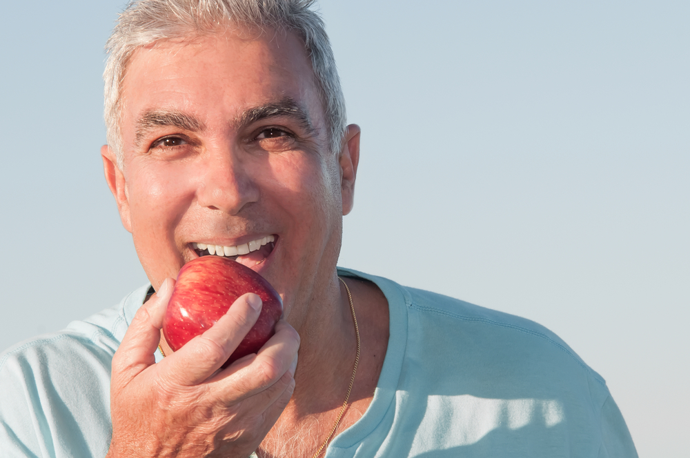 Man smiling, eating an apple after getting Cosmetic Dentures